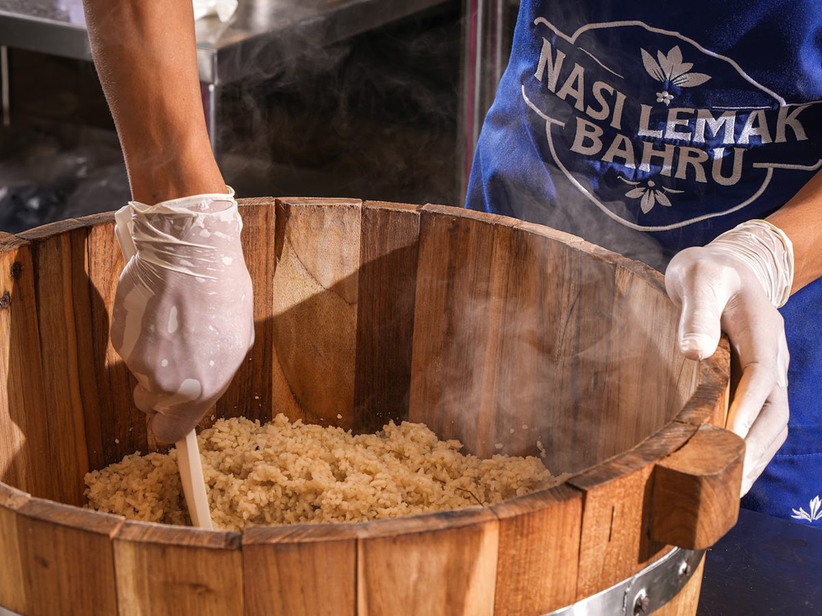 Coconut rice being folded by hand in a wooden steaming tub
