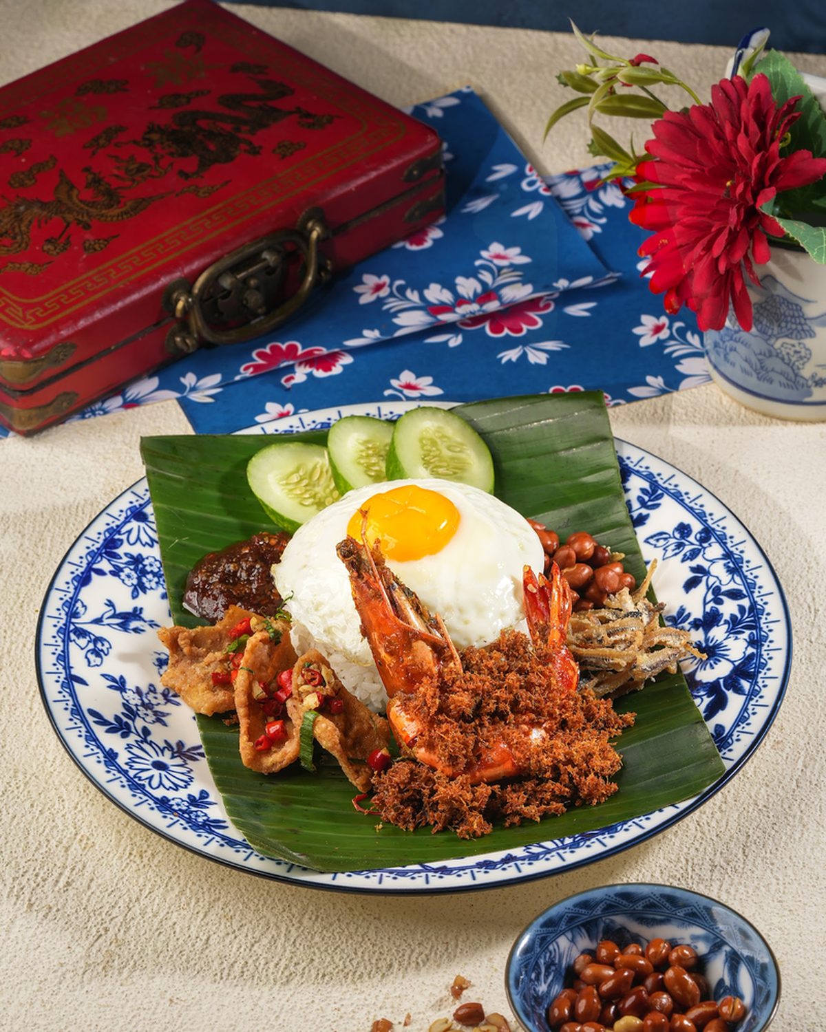 Nasi lemak on a Peranakan blue-and-white plate — coconut rice, sambal, egg and ayam rempah on banana leaf